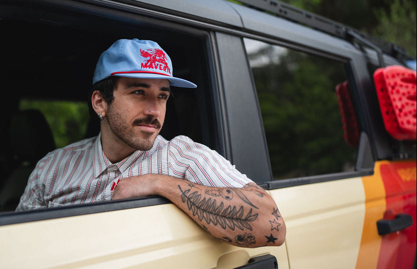 A stylish guy wearing a Maverik vintage unstructured hat in light blue and red with a horse design embroidered on the front